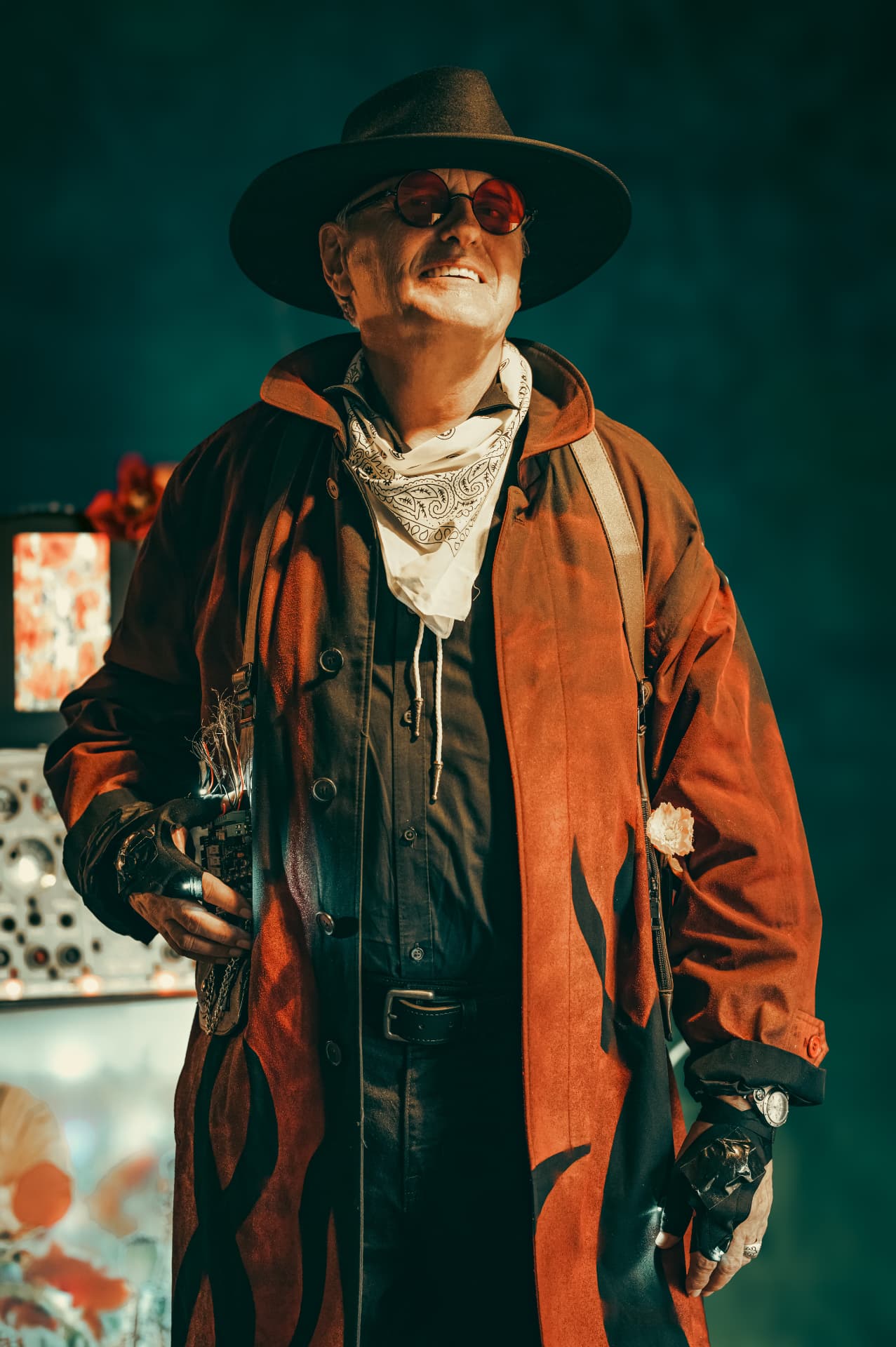 Chuck Wooke in a black hat, red glasses, white bandana and rust-colored coat, holding a wired device